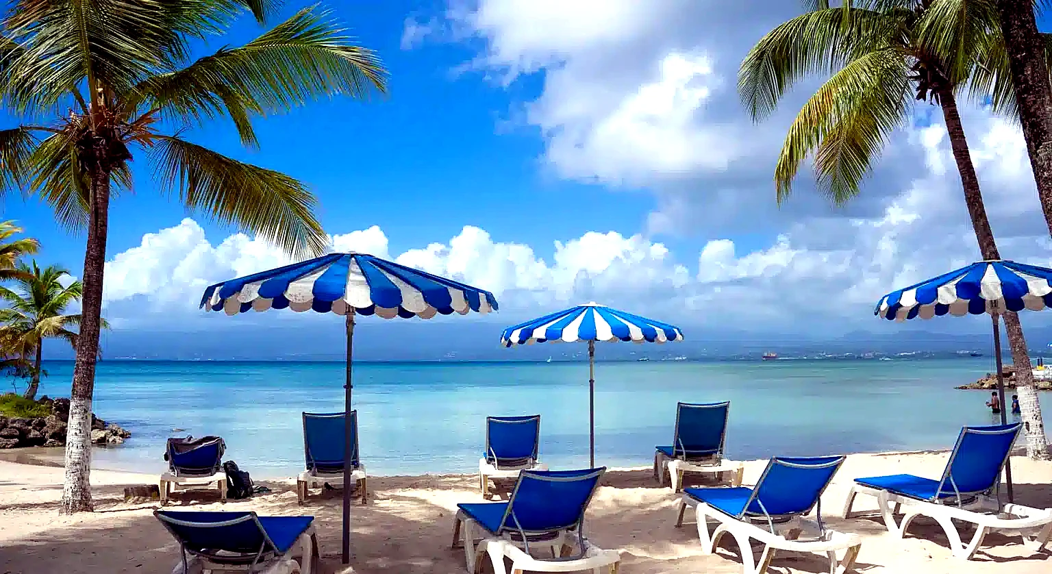 Plage du Gosier avec transats bleus, parasols rayés et cocotiers face au lagon turquoise